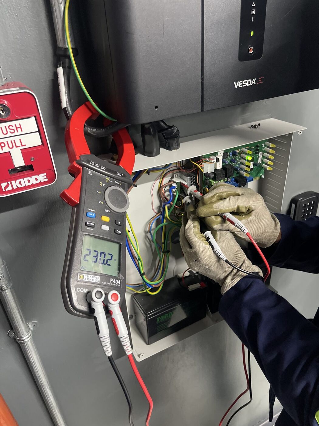 Engineer testing an aspirating smoke detection panel with a clamp meter