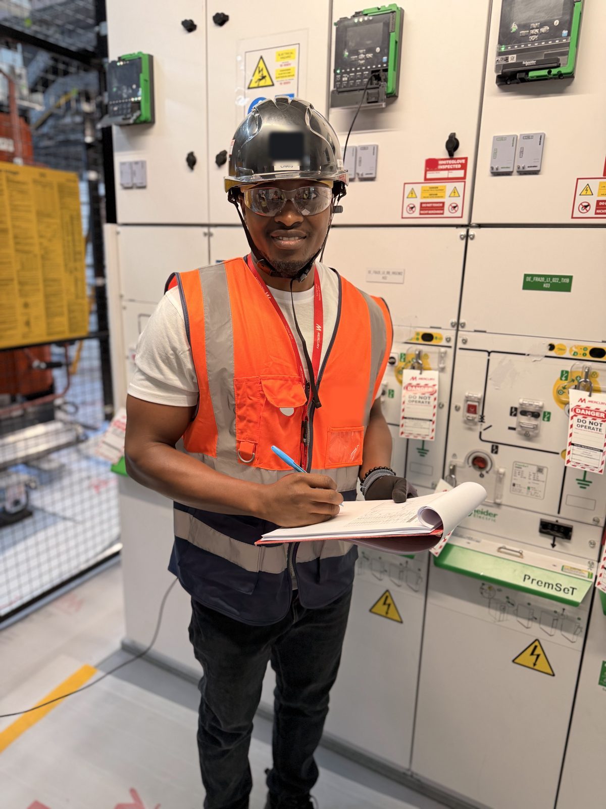 CurrenTSea engineer in hard hat, safety glasses and hi-vis completing test records beside locked-out MV switchgear